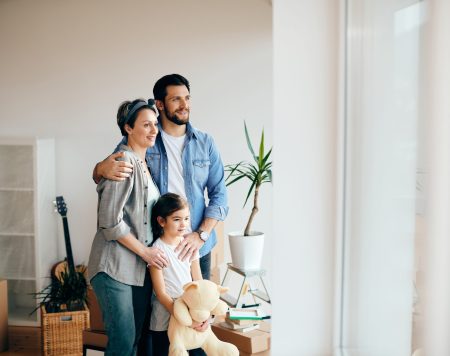 Happy parents with daughter enjoying at their new house and looking through the window. Copy space.
